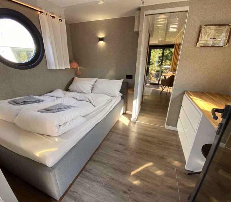Ein bequemes Bett und Blick vom Schlafzimmer auf die Natur und den Fluss in unserem Hausboot